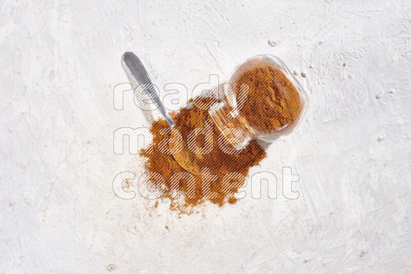 A glass jar full of ground paprika powder flipped with some spilling powder on white background