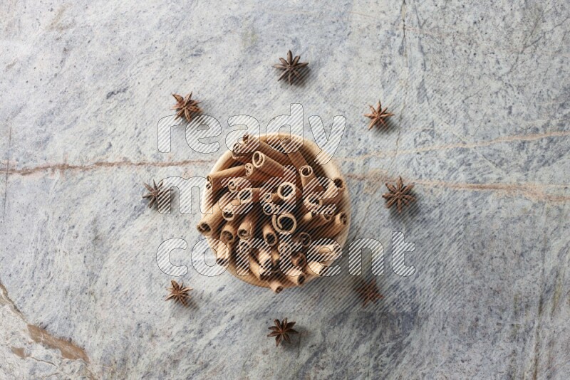 wooden bowl full of cinnamon sticks surrounded by star anis on marble background in different angles