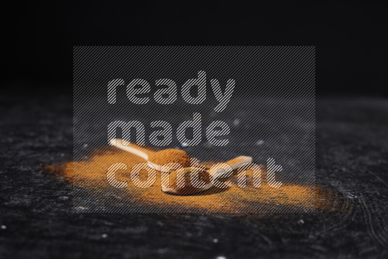 Two wooden spoons full of ground paprika powder on black background