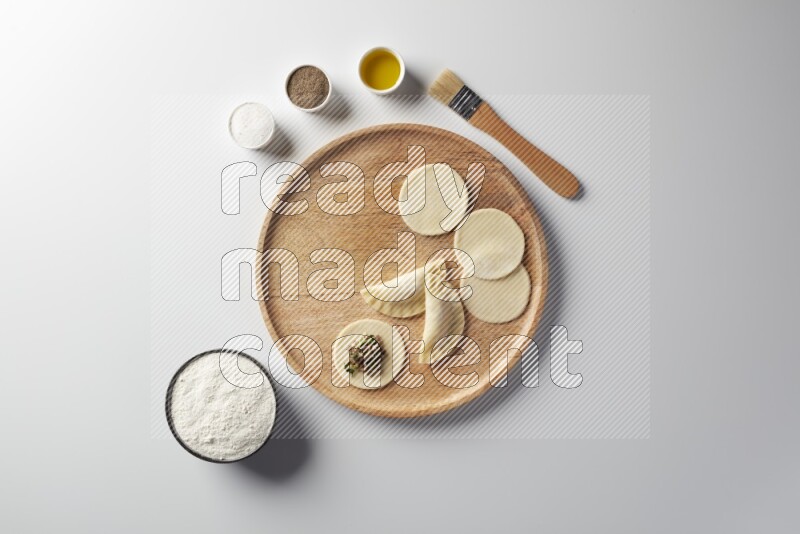 two closed sambosas and one open sambosa filled with meat while flour, salt, black pepper and oil with oil brush aside in a wooden dish on a white background