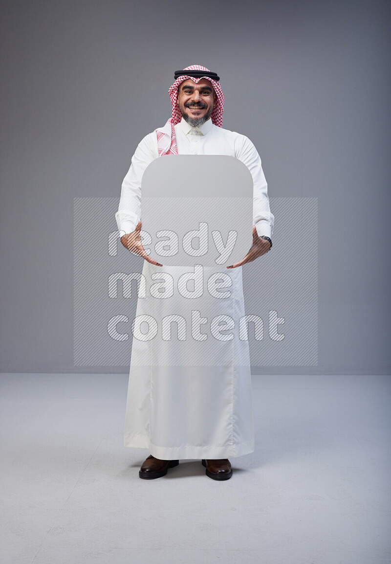 Saudi man Wearing Thob and red Shomag standing holding social media sign on Gray background