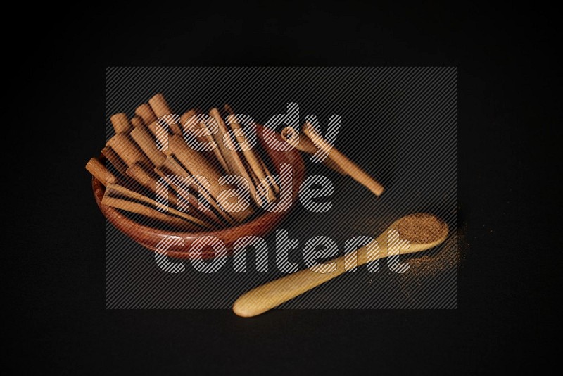 Cinnamon sticks in wooden bowl and cinnamon powder in a wooden spoon on black background