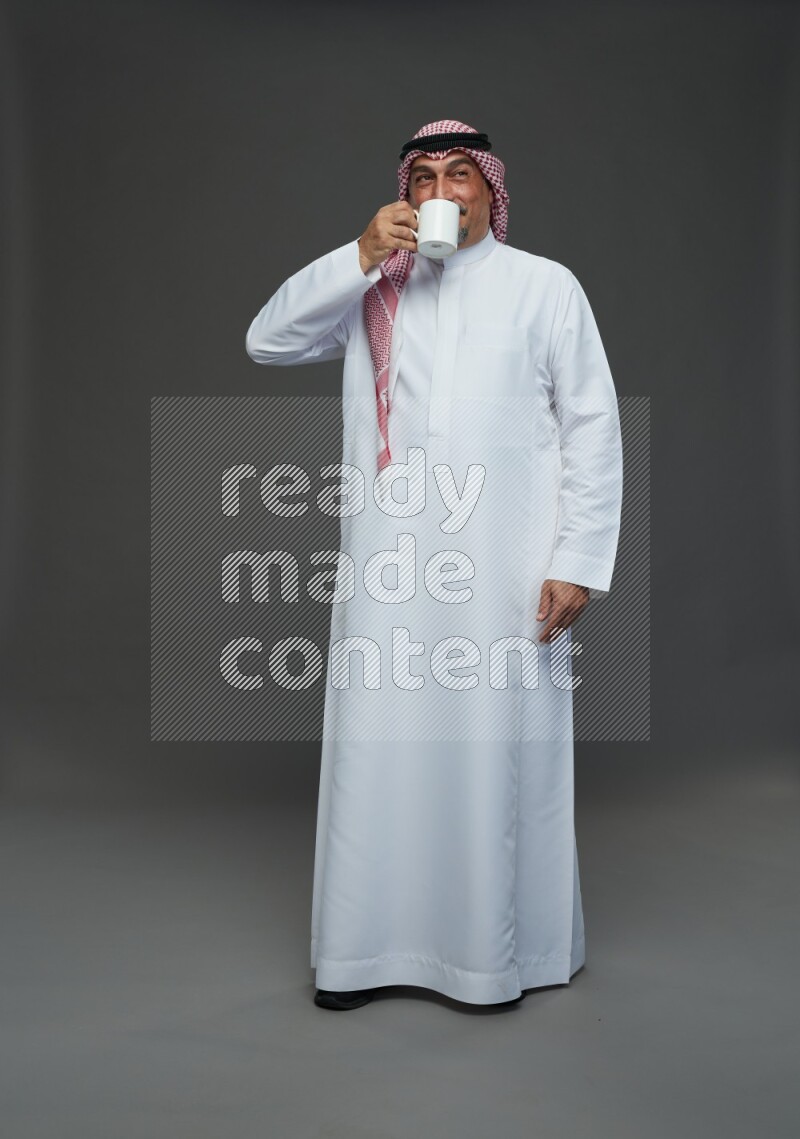 Saudi man with shomag Standing holding mug on gray background
