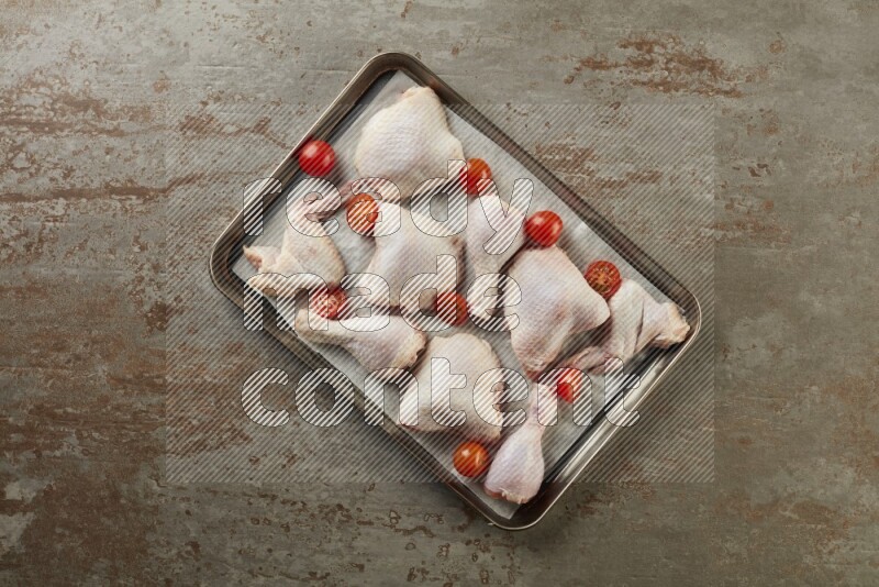 Mixed fresh chicken pieces in an oven tray on a textured rustic background