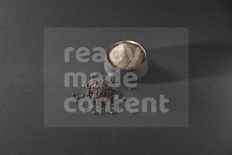 بودرة الفلفل الأسود في وعاء فخاري أسود مع حبوب الفلفل الأسود بجانبها علي خلفية سوداء