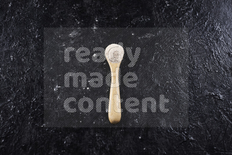 A wooden spoon full of onion powder on black background