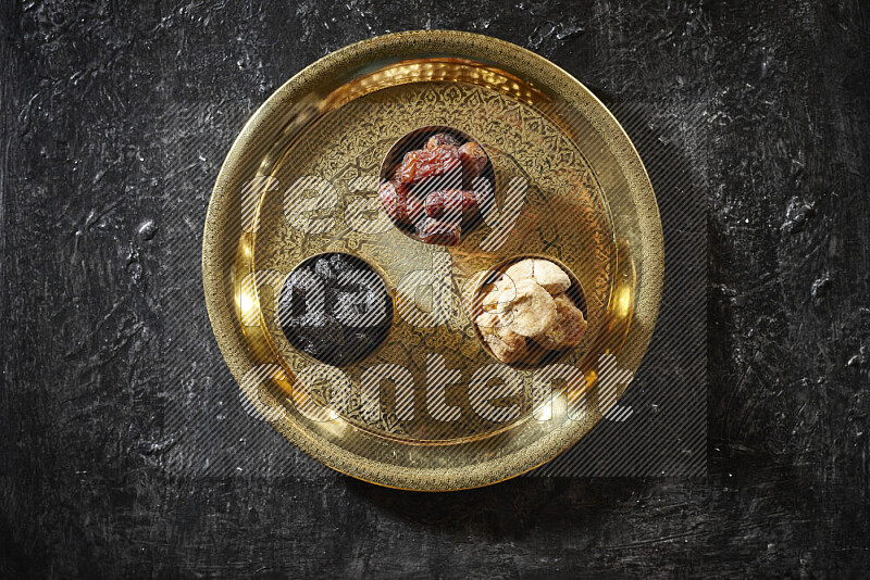 Dried fruits in metal bowls on a tray in a dark setup
