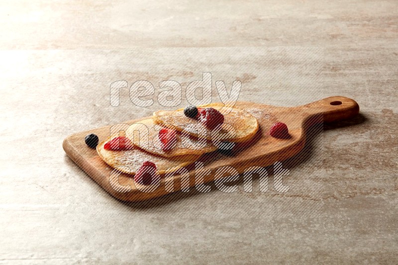 Three stacked mixed berries pancakes on a wooden board on beige background