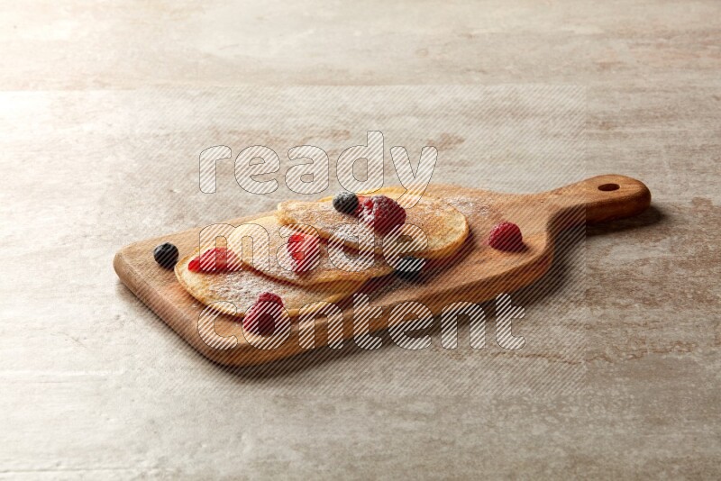 Three stacked mixed berries pancakes on a wooden board on beige background