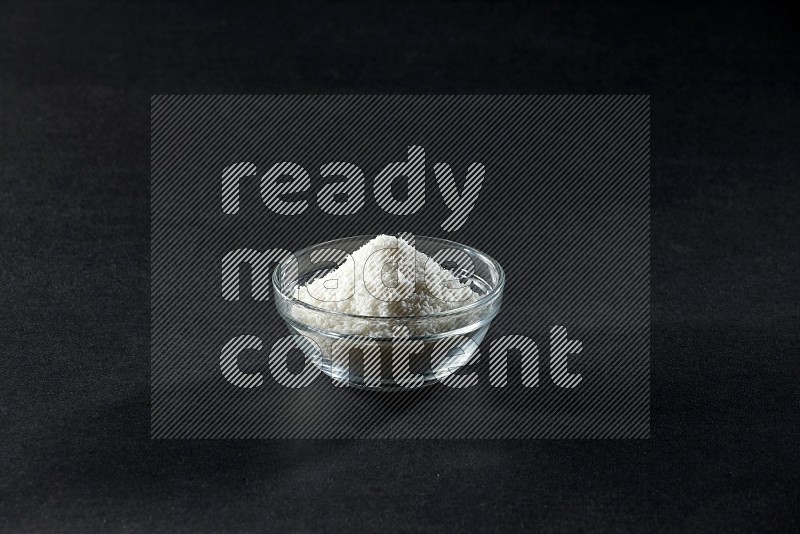 A glass bowl full of desiccated coconut on a black background in different angles
