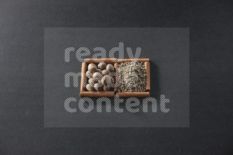 مربعان من أعواد القرفة ممتلئان بجوزة الطيب وحبوب الفلفل الأبيض علي خلفية سوداء