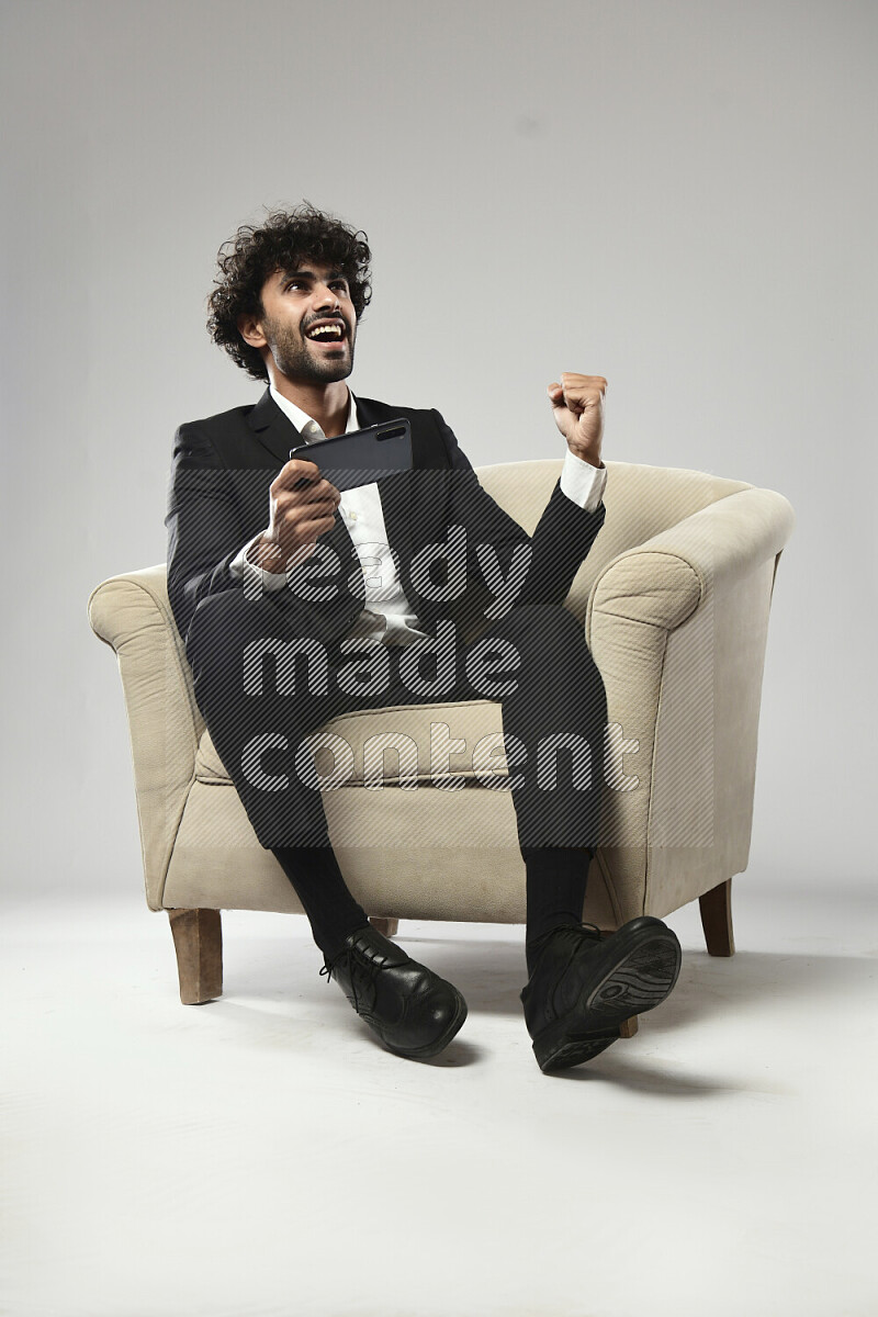 رجل يرتدي ملابس رسمية يجلس علي كرسي و يلعب علي الهاتف علي خلفية بيضاء