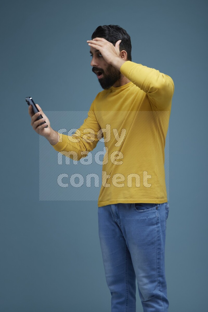 Man typing on his phone in a blue background wearing a yellow shirt