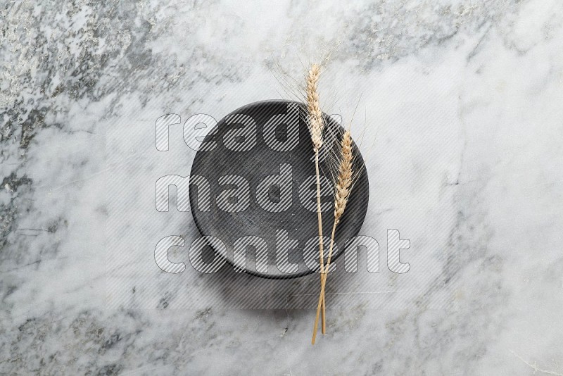 Wheat stalks on Black Pottery Plate on grey marble flooring, Top view