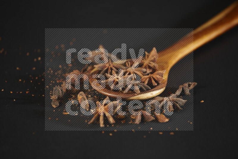 يانسون نجمي في مغرفة خشبية مع المزيد من اليانسون على خلفية سوداء