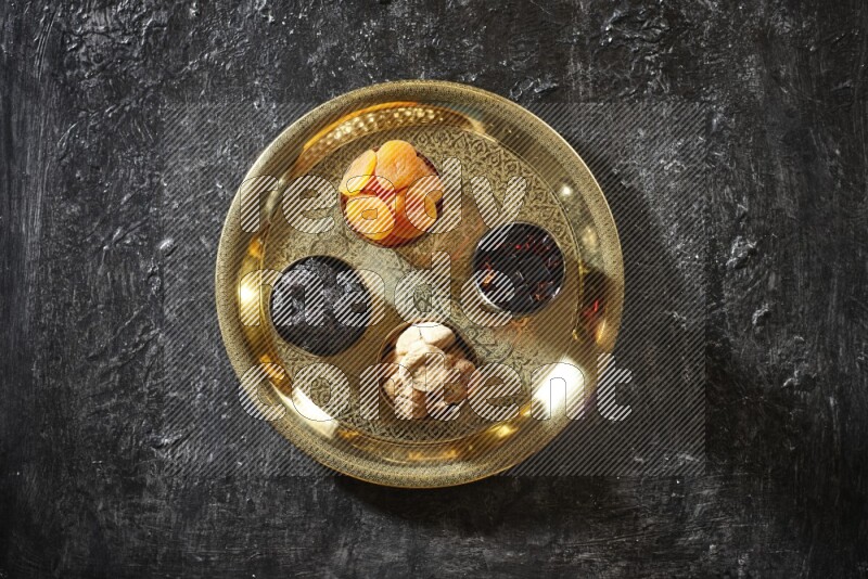 Dried fruits in metal bowls with tamarind on a tray in dark setup