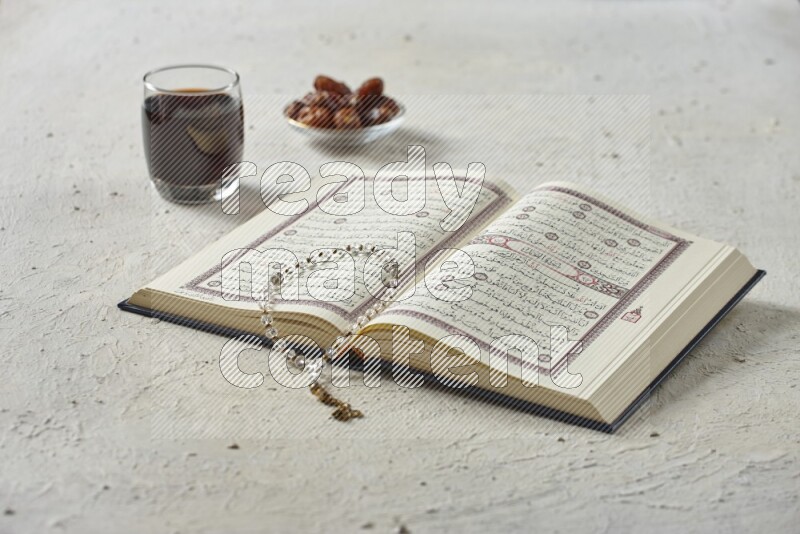 Quran with dates, prayer beads and different drinks all placed on textured white background