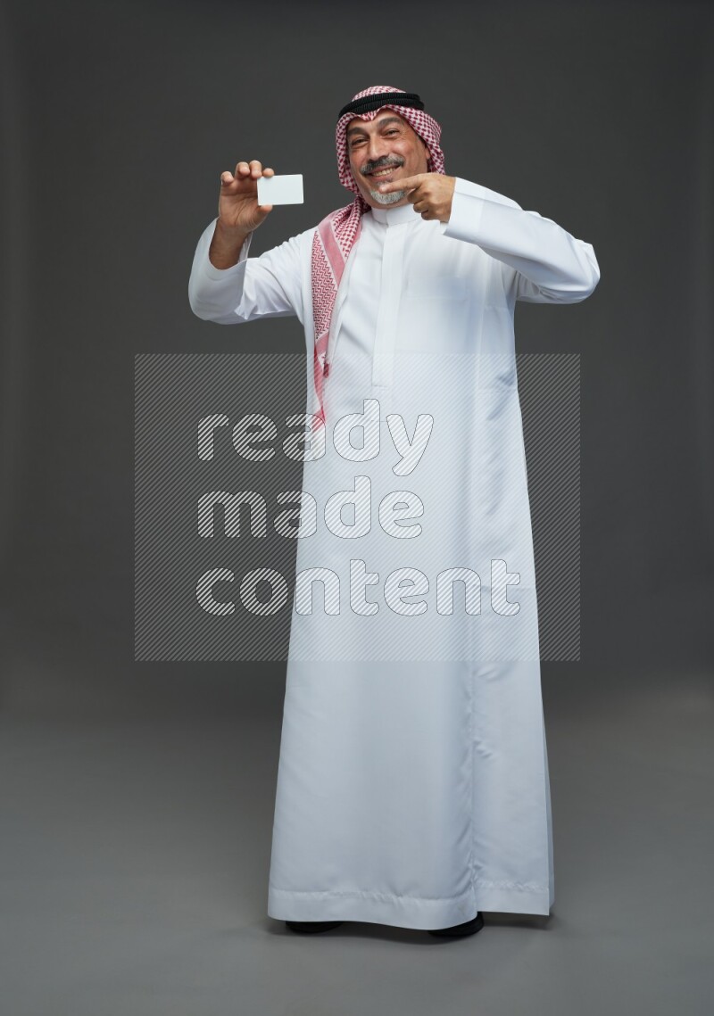 Saudi man with shomag Standing holding ATM card on gray background