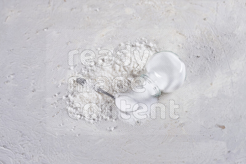 A glass jar full of table salt with some sea salt crystals beside it on a white background