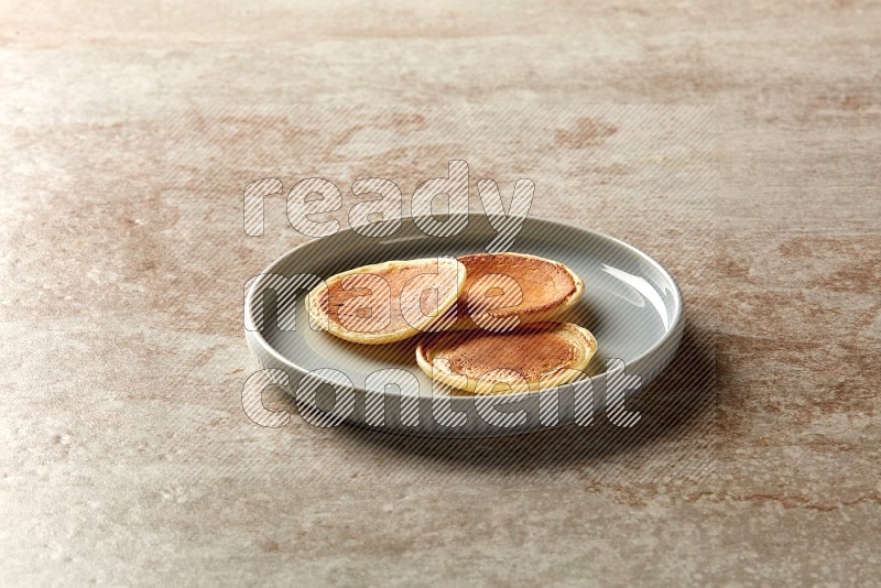 Three stacked plain mini pancakes in a blue plate on beige background