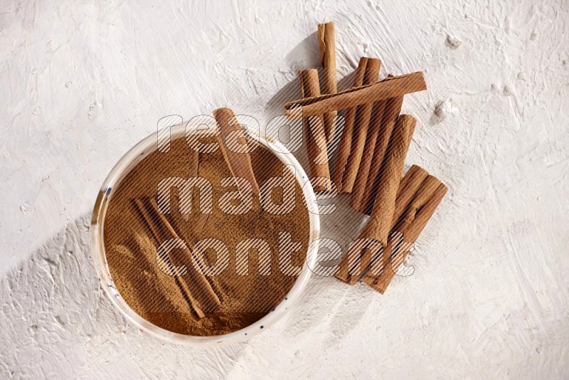 Ceramic bowl full of cinnamon powder with cinnamon sticks on the side on white background