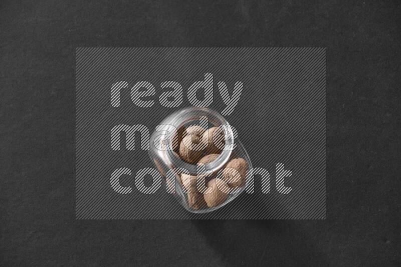 A glass spice jar full of nutmeg on black flooring