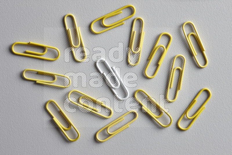 A white paperclip surrounded by bunch of yellow paperclips on grey background