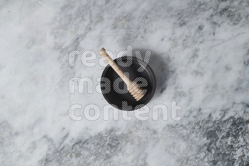 Black Pottery Oven Plate with wooden honey handle in it, on grey marble flooring, Top View