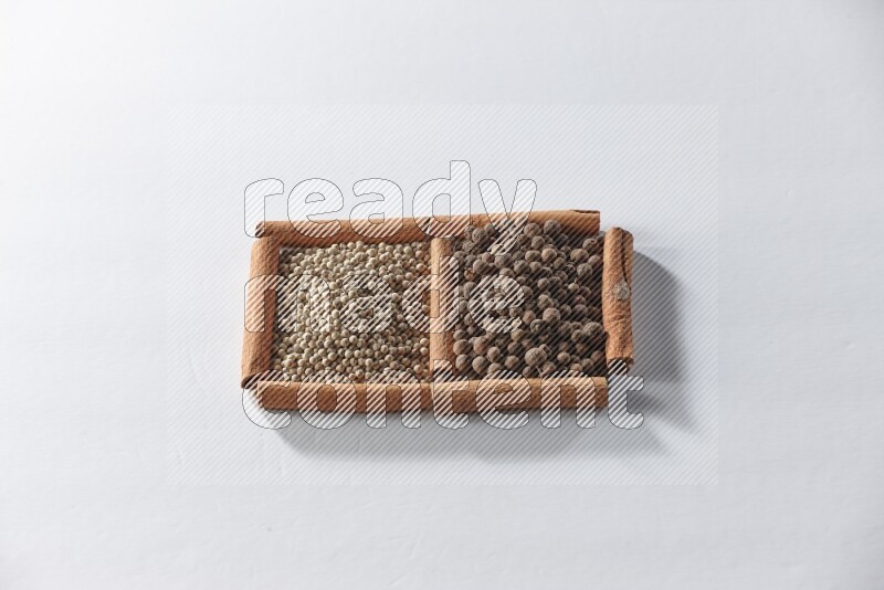 مربعان من أعواد القرفة ممتلئان بحبوب الفلفل الأبيض وحبوب الفلفل الحلو علي خلفية بيضاء