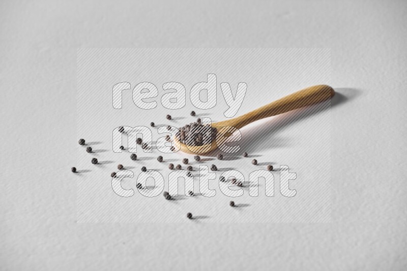 حبوب الفلفل الأسود في ملعقة خشبية علي خلفية بيضاء