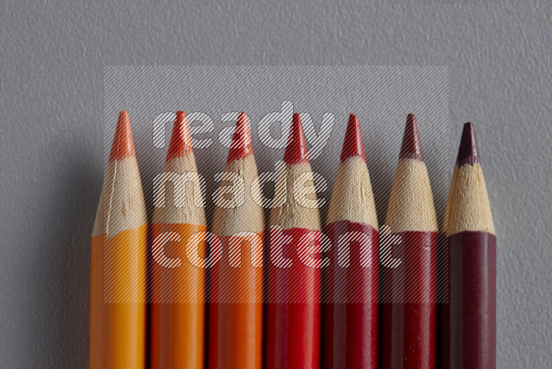 A collection of colored pencils arranged showcasing a gradient of orange and red hues on grey background