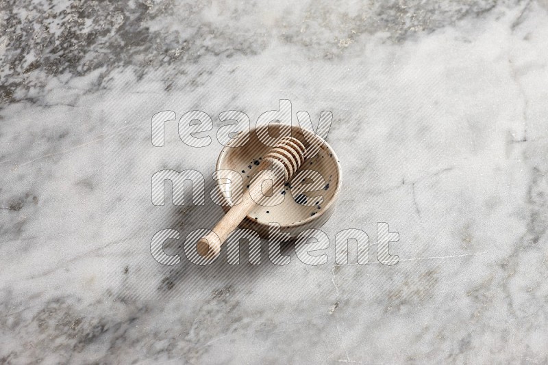 Multicolored Pottery bowl with wooden honey handle in it, on grey marble flooring, 65 degree angle