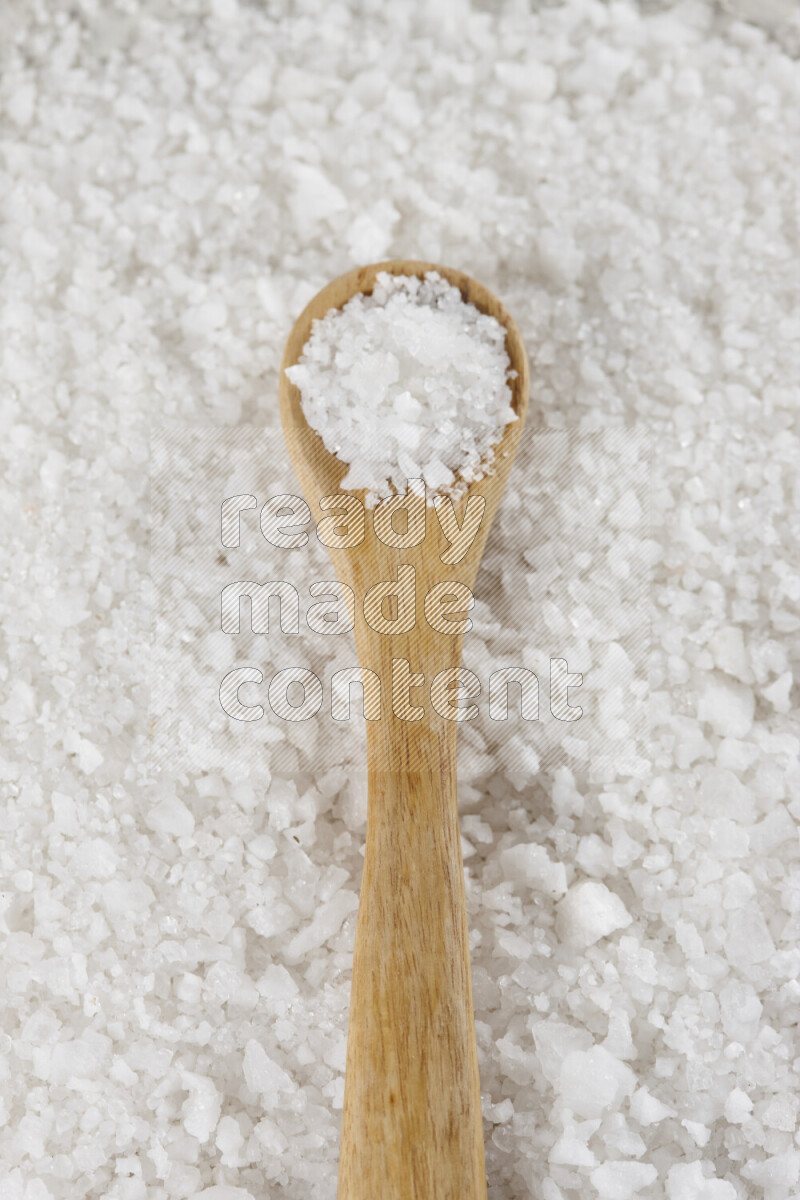 A wooden spoon full of white salt on white background