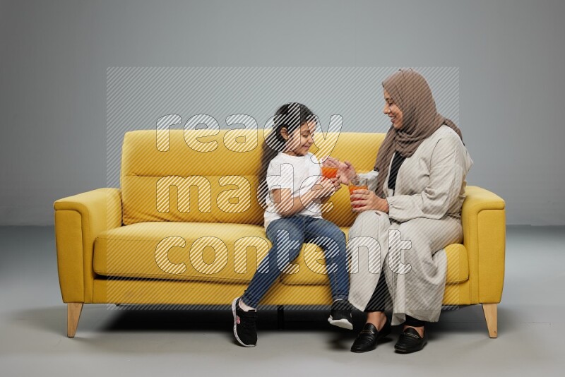 Mom and daughter sitting drinking juice on gray background