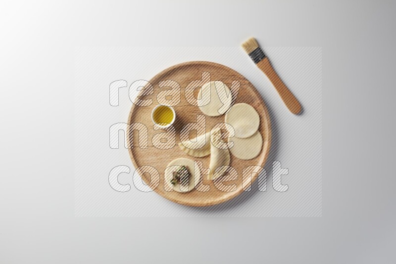 two closed sambosas and one open sambosa filled with meat while oil with oil brush aside in a wooden dish on a white background