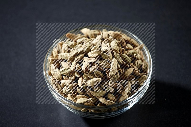 A glass bowl full of cardamom on black flooring