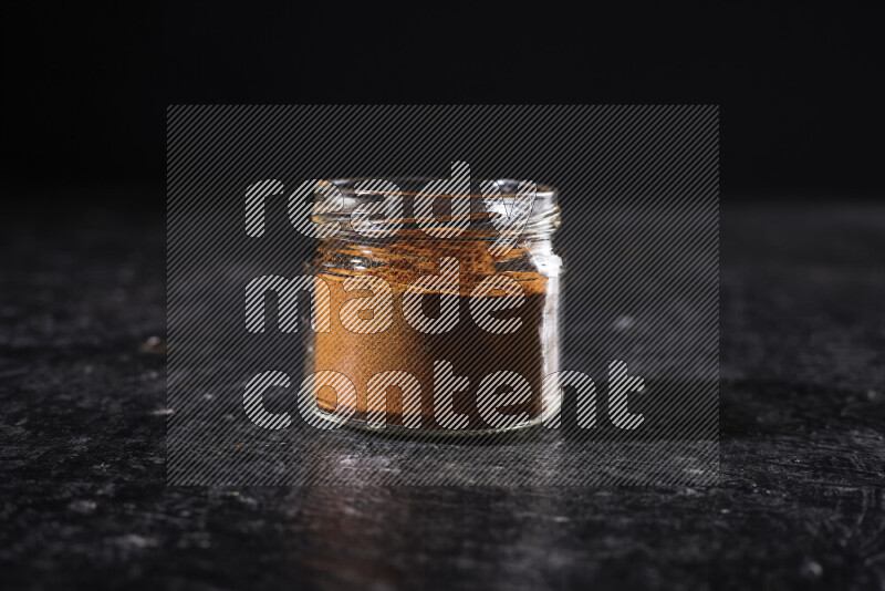 A glass jar full of ground paprika powder on black background