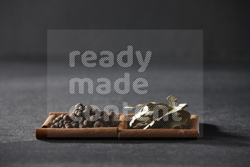 مربعان من أعواد القرفة ممتلئان ببهار الفلفل الحلو وأوراق الغار علي خلفية سوداء