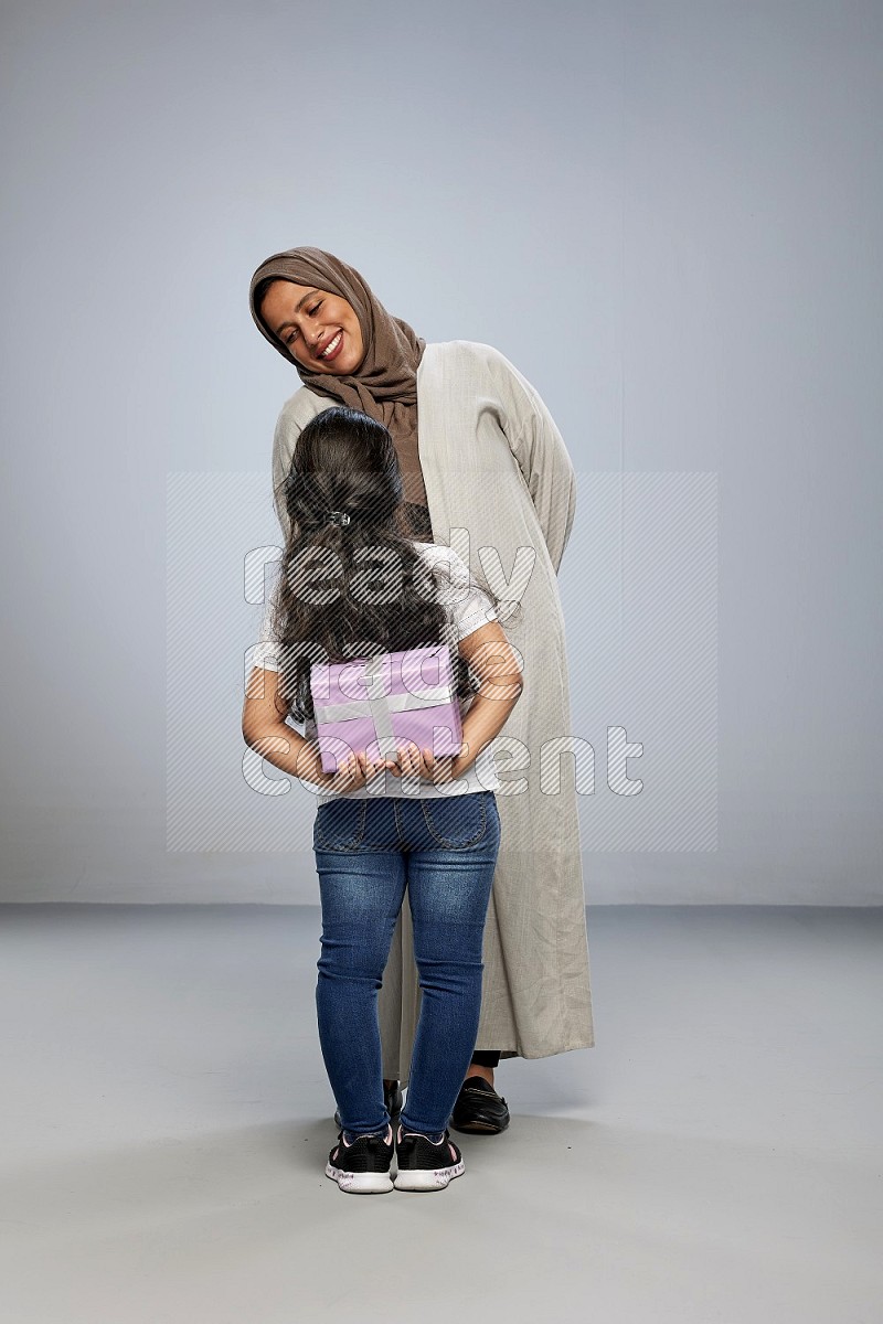 A girl standing hiding a gift behind her back for her mother on gray background