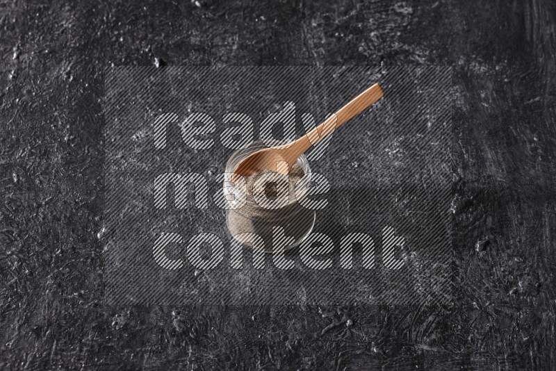 بودرة الفلفل الأسود في وعاء زجاجي مع ملعقة خشبية علي خلفية سوداء