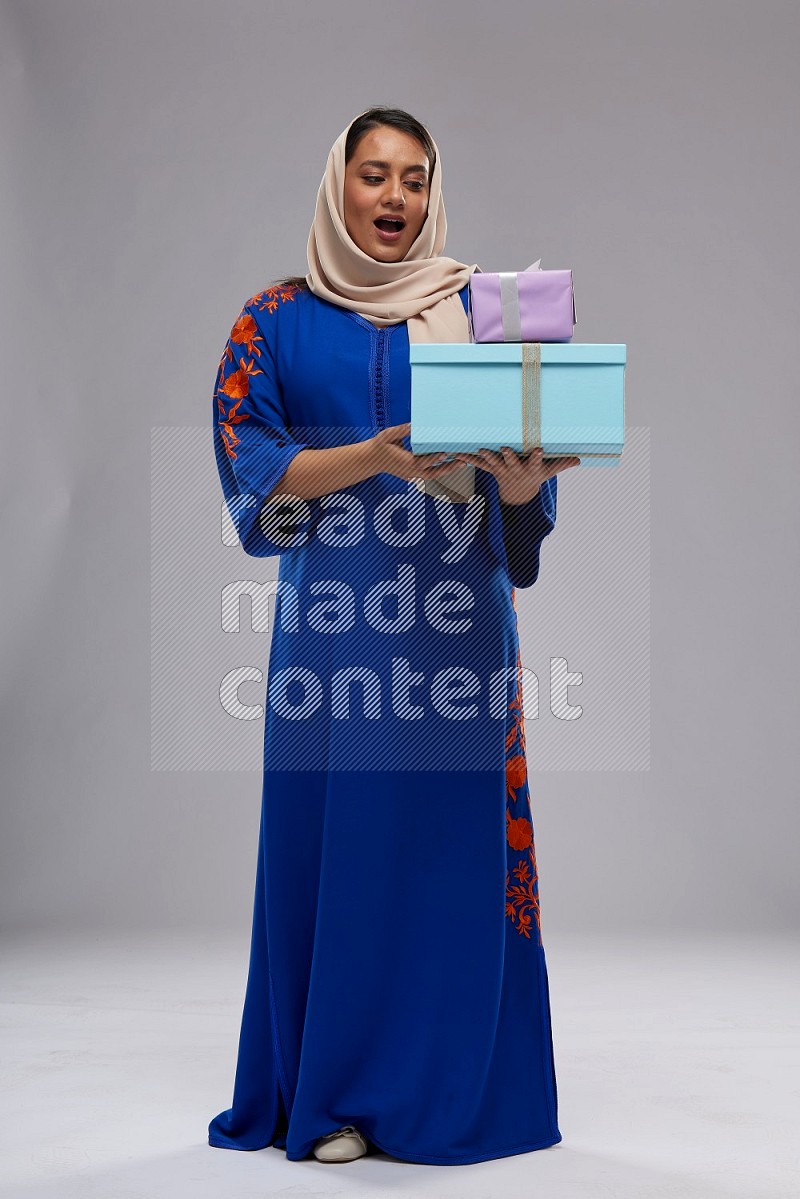 A Saudi woman standing wearing Jalabeya holding a gift box