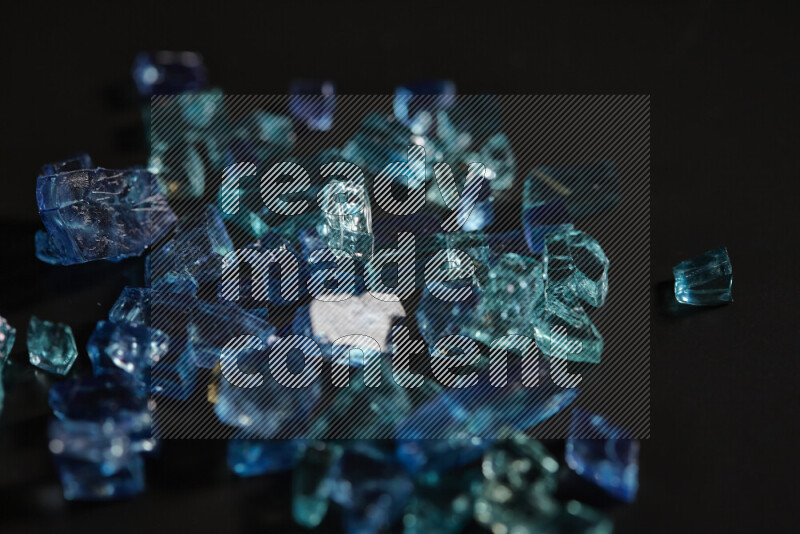 Transparent blue fragments of glass scattered on a black background