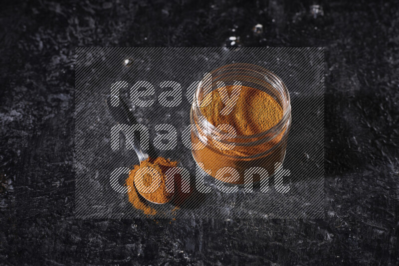 A glass jar full of ground paprika powder on black background