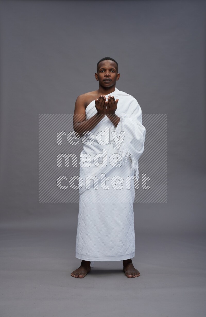A man wearing Ehram Standing dua'a on gray background