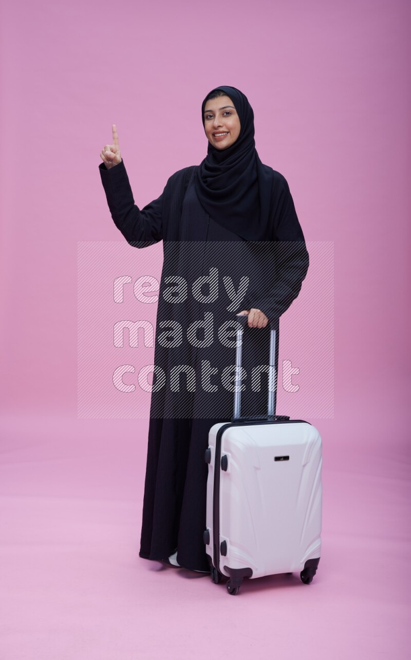 Saudi woman wearing Abaya standing holding bag on pink background