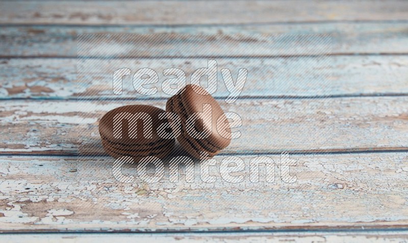 45º Shot of two Brown Dark Chocolate macarons on light blue wooden background