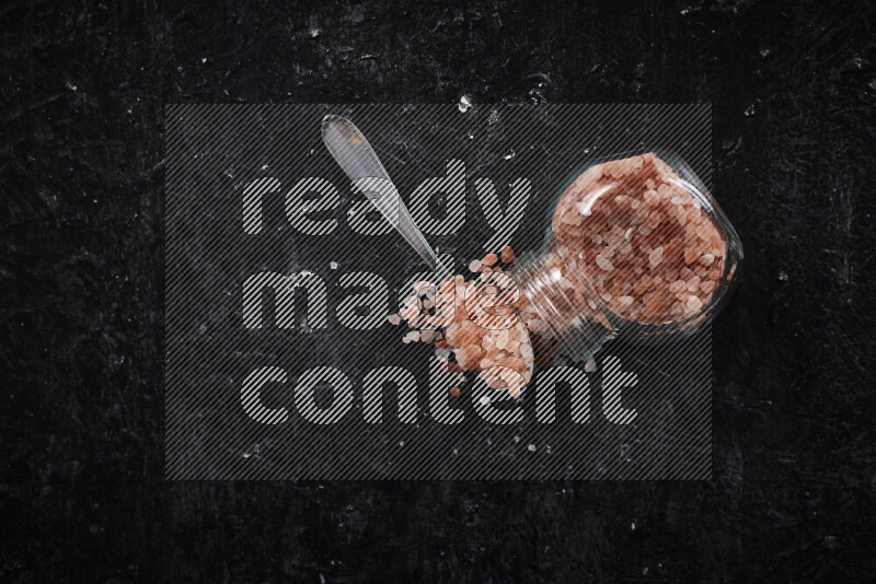 A glass jar full of coarse himalayan salt crystals on black background