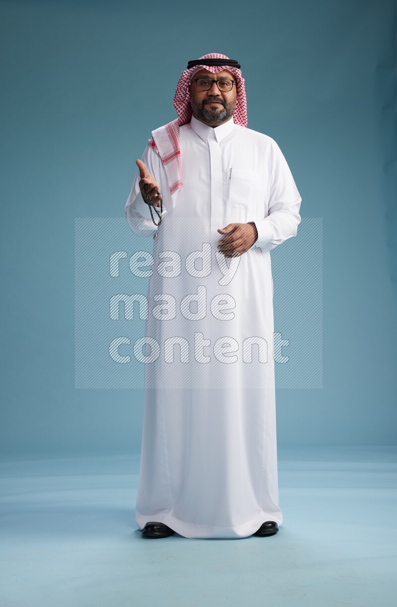 Saudi Man with shimag Standing Interacting with the camera on blue background