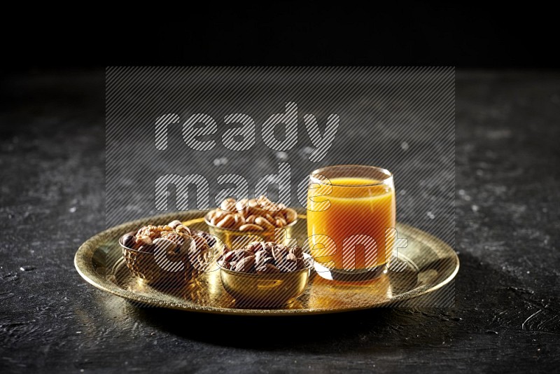 Nuts in metal bowls with qamar eldin on a tray in dark setup