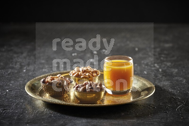 Nuts in metal bowls with qamar eldin on a tray in dark setup